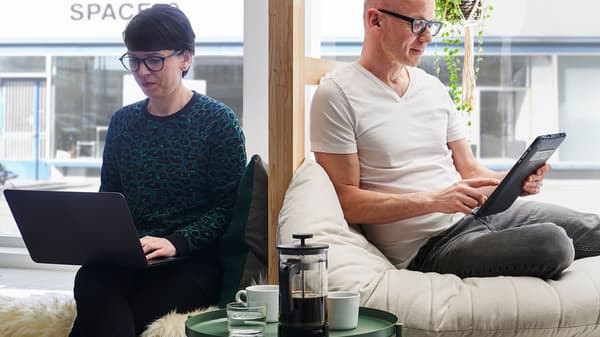 A woman with a laptop on her lap sits next to a man holding a touchscreen.