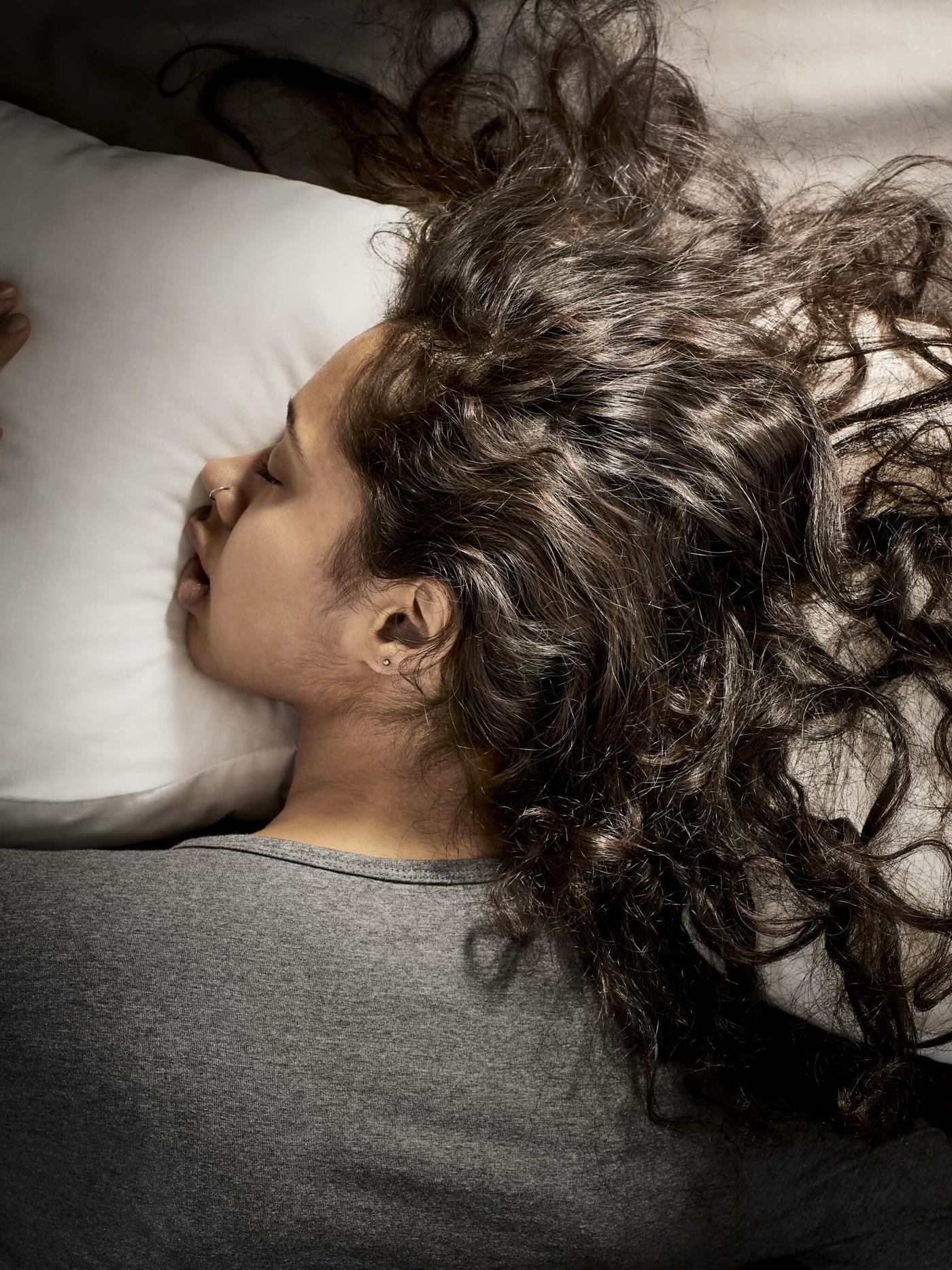 A woman with brown curly lying face down on a pillow sleeping comfortably.