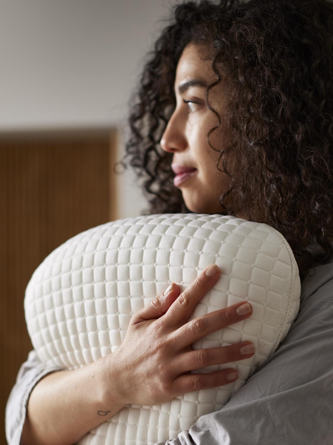 A woman with brown hair and white shirt sleeping under a white blanket on a ROSENSKÄRM ergonomic pillow.