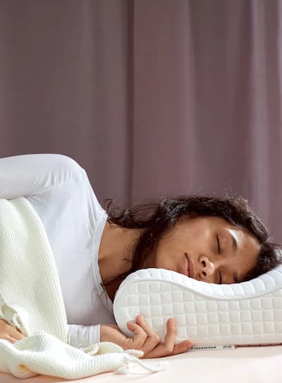 A woman with brown hair and white shirt sleeping under a white blanket on a ROSENSKÄRM ergonomic pillow.