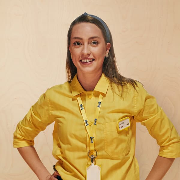 A woman with brown hair smiles while wearing a yellow IKEA co-worker collared shirt, lanyard and name tag.