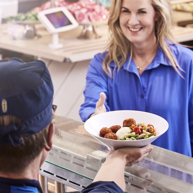 A woman with long blonde hair and a blue shirt is handed a white plate of food