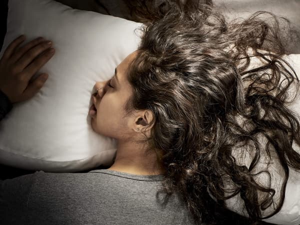 A woman with long curly hair lying on her stomach on a white pillow.