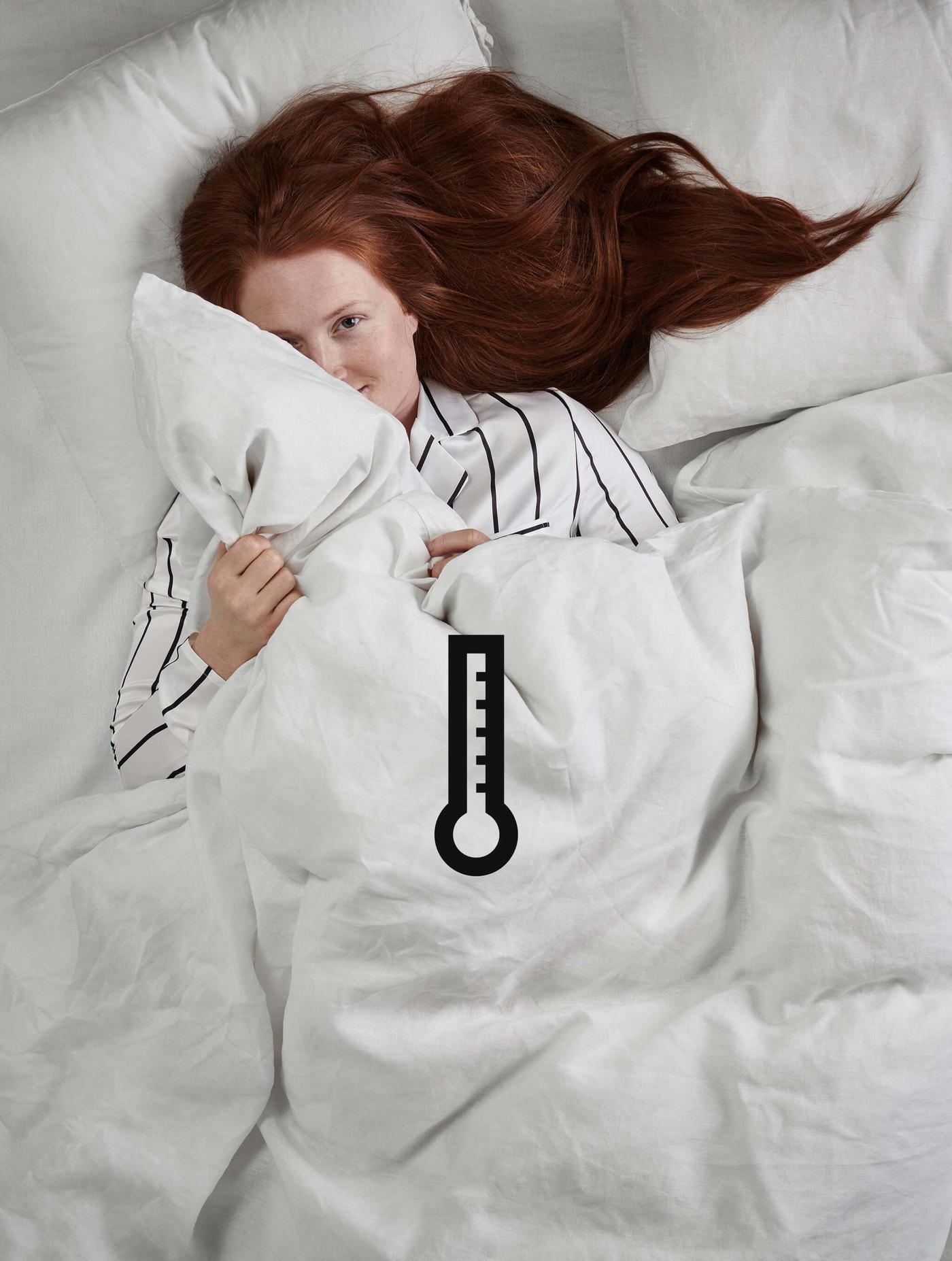 A woman with red hair laying in a bed with a white comforter and white pillows.