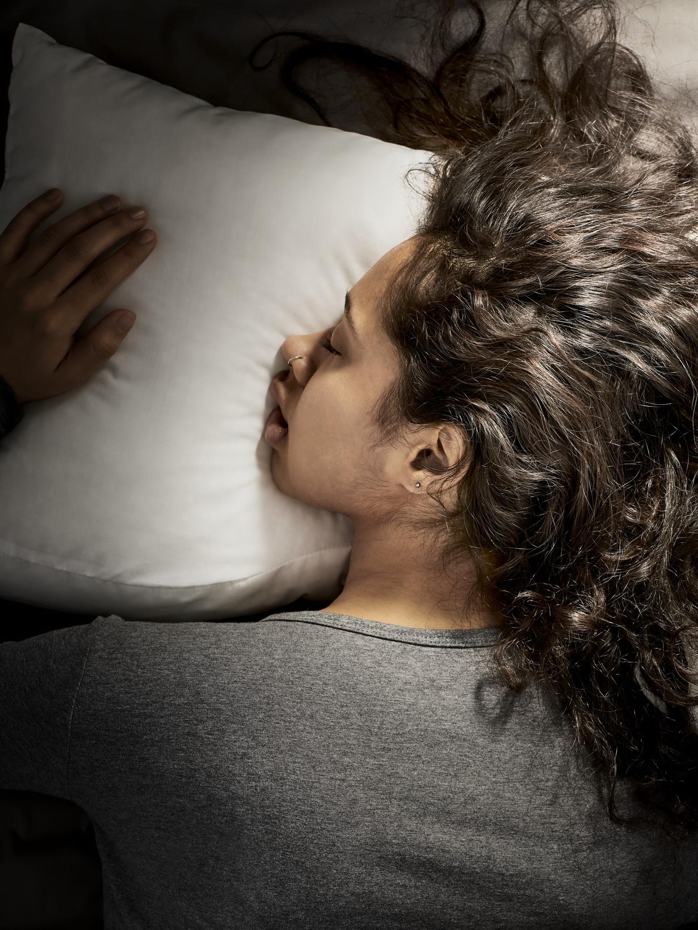 A woman with red hair laying in a bed with a white comforter and white pillows.