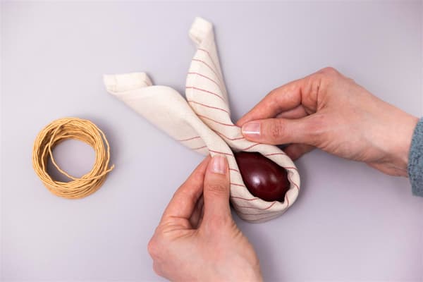 A woman wraps the rolled-up napkin around an egg.