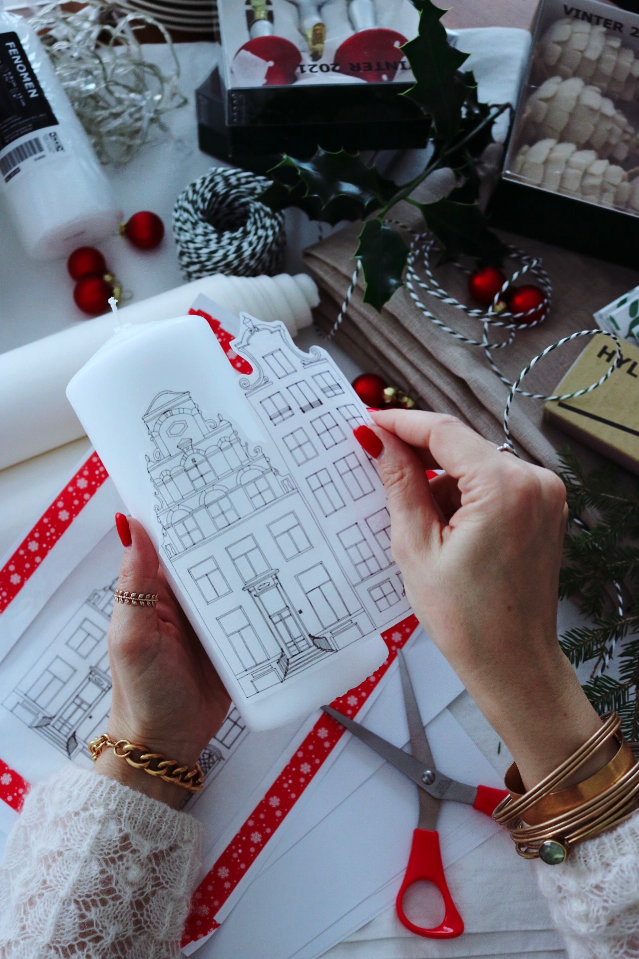 A women is attaching a print of houses to a white candle