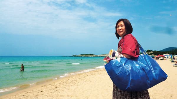 A women standing on a beach and holding ikea frakta bag on her shoulder