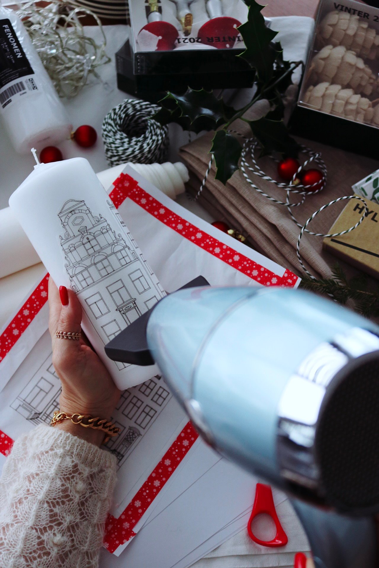 A womens hand holding the white candle, while she uses the blow dryer to attach the print