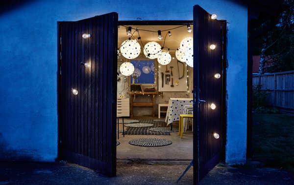 A wood backyard doorway with glowing string lights open to show a festive New Years party with dotted paper lanterns inside.