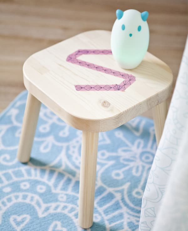 A wood stool turned bedside table for a child’s bedroom is personalised with washi tape. A nightlight sits on the stool.