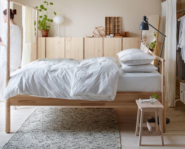 A wooden bed frame with white bedding.