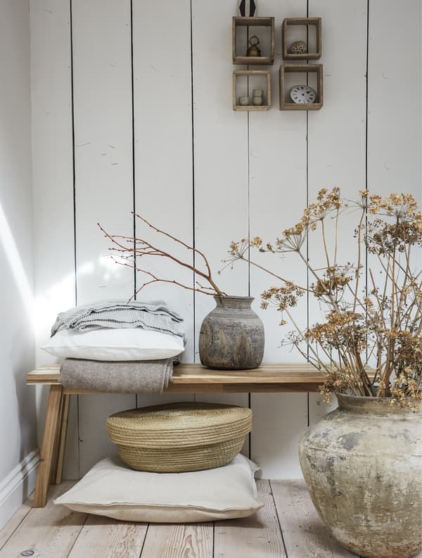 A wooden bench surrounded by rustic pots, dried foliage and natural textures.