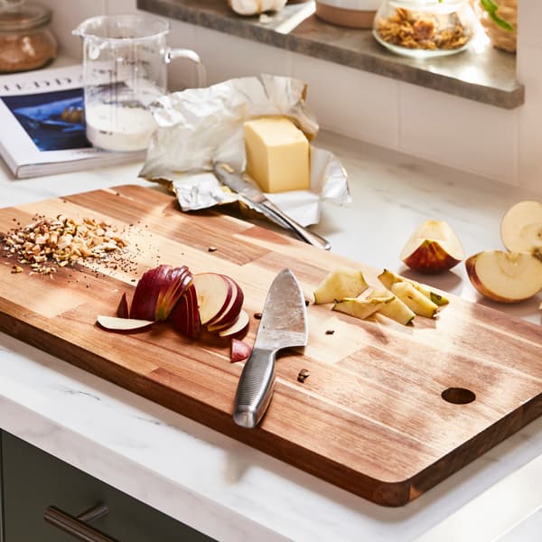 A wooden chopping board with a knife and red applees and nuts on it.