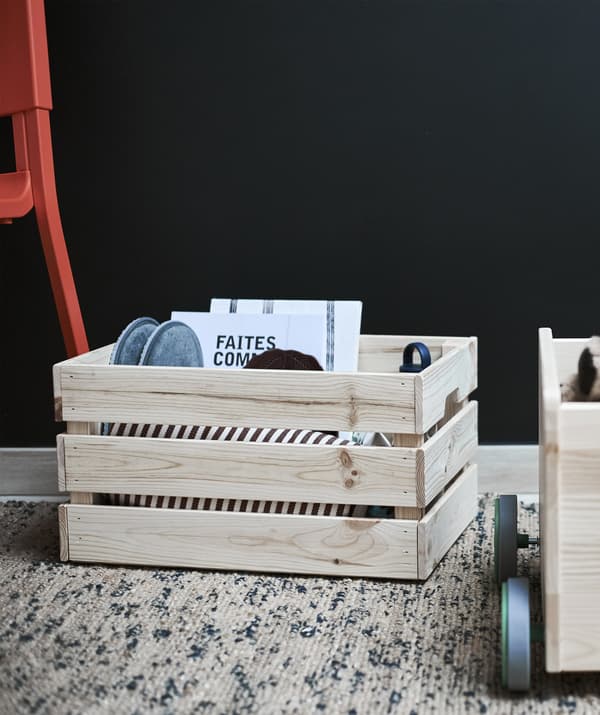 A wooden crate filled with objects against a dark wall.