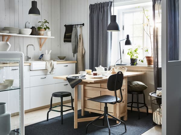 A wooden dining table with drop leaves in a kitchen with white cabinets and a wood countertop.