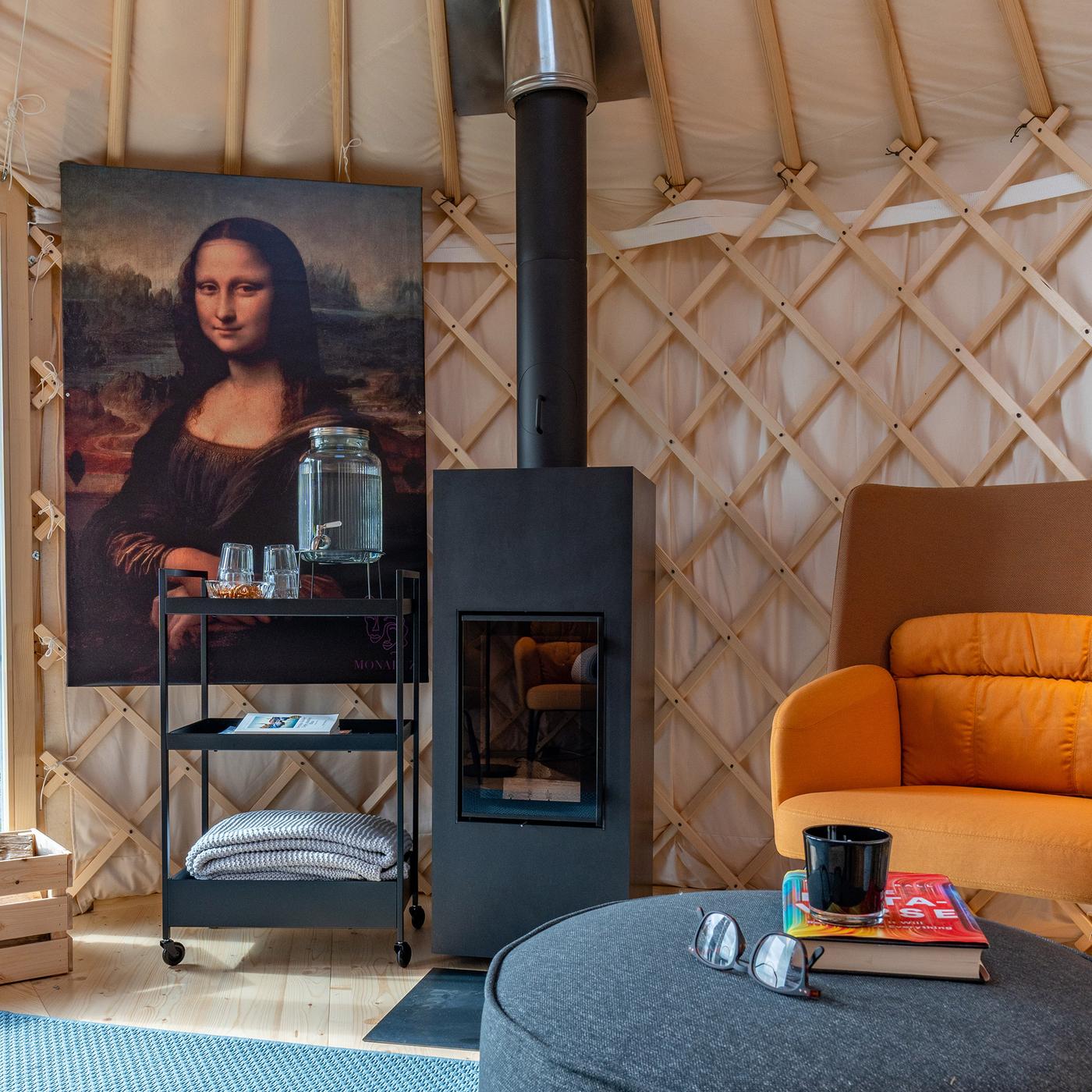 A wooden fireplace in a yurt, which stands next to a large painting of the Mona Lisa and an armchair with a side table