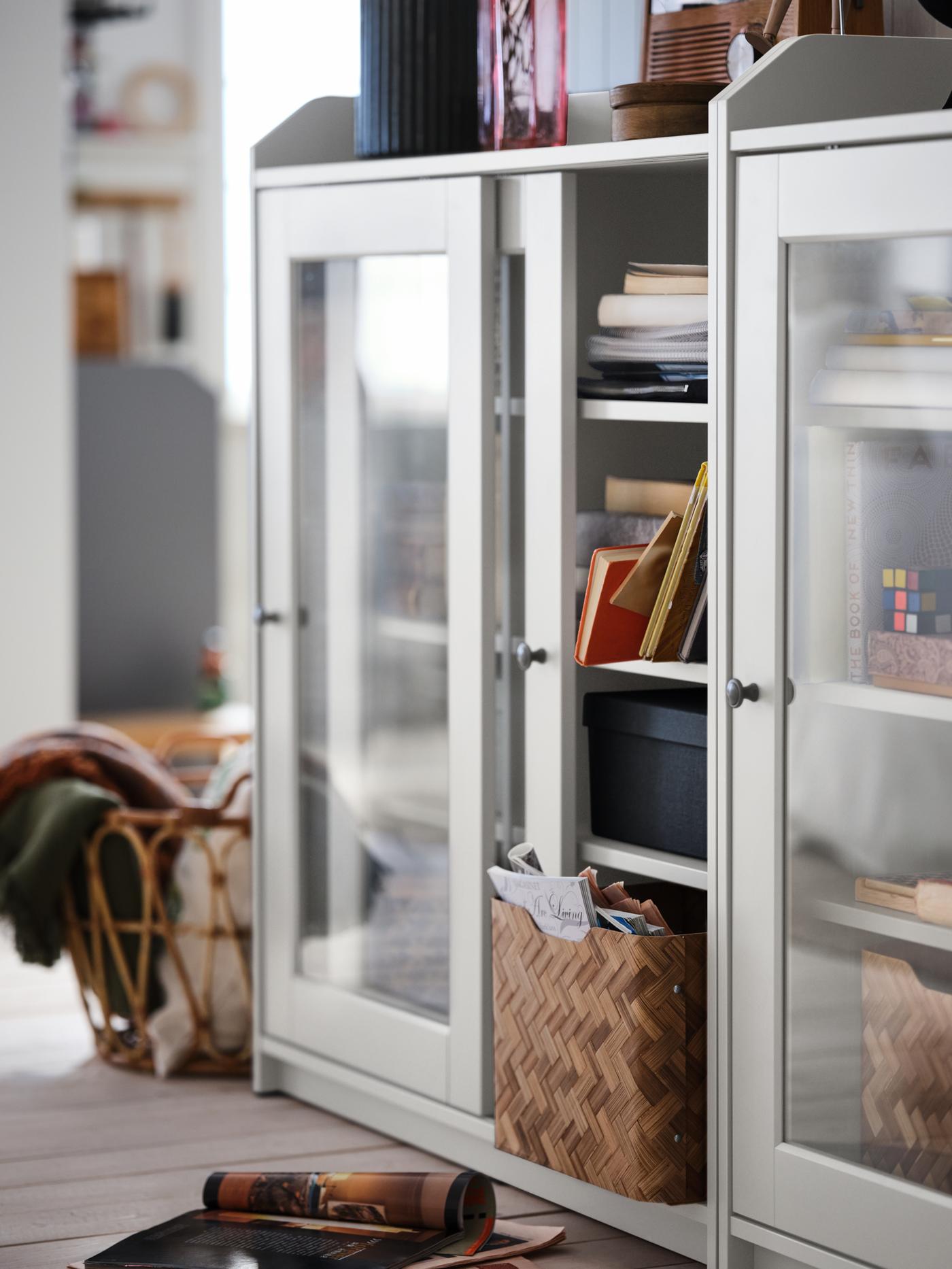A wooden-floor room with a white HAUGA glass-door cabinet filled with everyday storage inside and a decorative display on top.