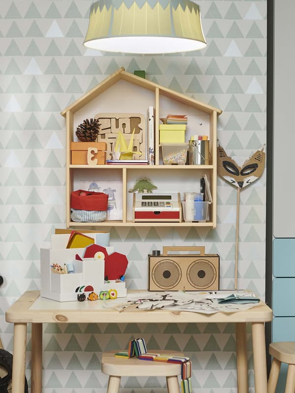 A wooden kids table with arts and crafts sitting on it and a wall house decor holding craft items in it.