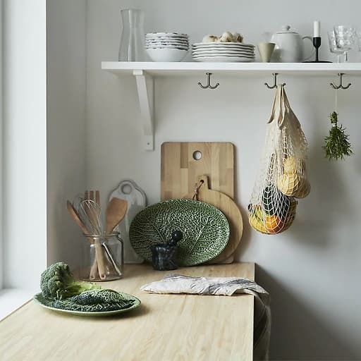 A wooden kitchen worktop with leaf-shaped plate, wooden chopping boards and tableware on a shelf.
