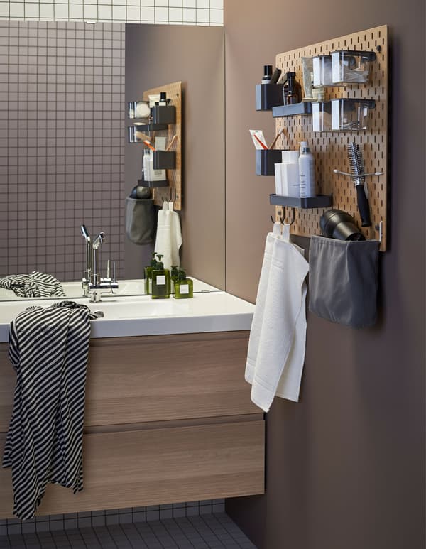 A wooden SKÅDIS pegboard next to a wash basin in a bathroom with accessories to hold toothbrushes, towels and other toiletries