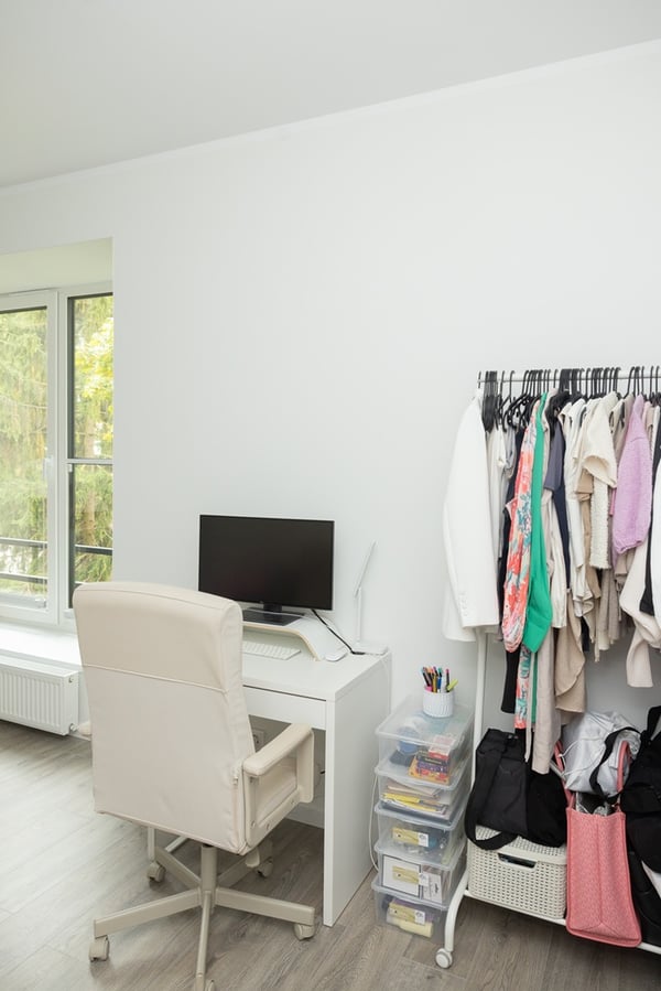 A work area with a desk and chair, with a clothes rail placed nearby.