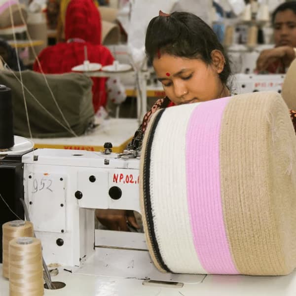 A worker operates a sewing machine, crafting a large spool of fabric with beige and pink stripes.