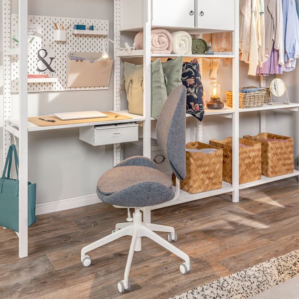 A workspace is set up in a bedroom using a storage system as a desk, a pegboard to store office supplies, and a swivel chair.