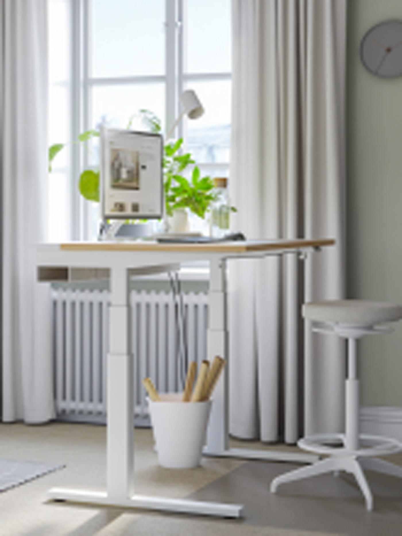A workspace with a MITTZON desk in white and oak veneer, placed next to a large window with potted plants.