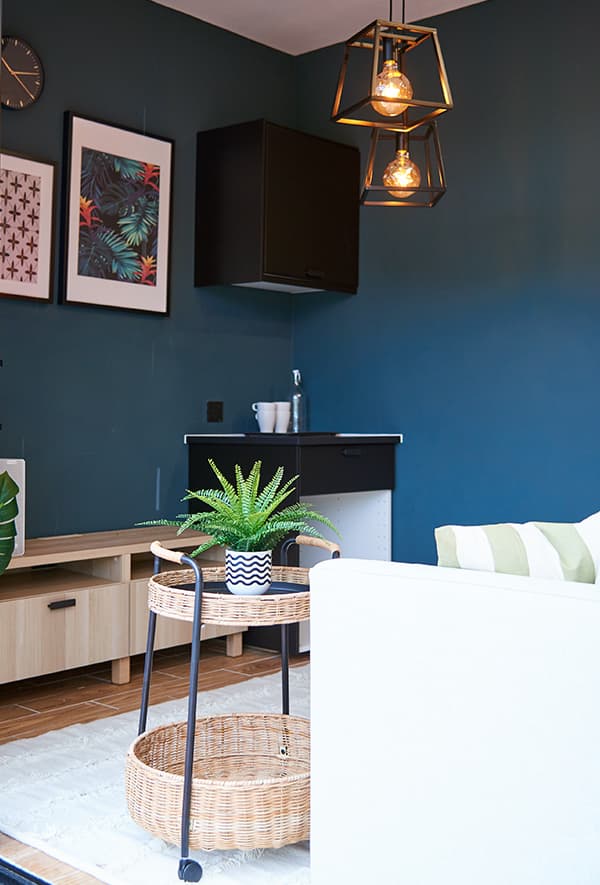 A woven trolley table with a potted plant on top in a dark blue room.