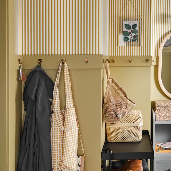 A yellow and white/striped wall with many small, brass-coloured hooks where clothes, keys and accessories hang.