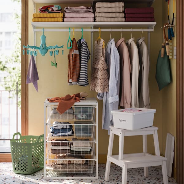 A yellow bathroom with a white BOAXEL wardrobe combination has white boxes on shelves and clothes hanging from a rail.