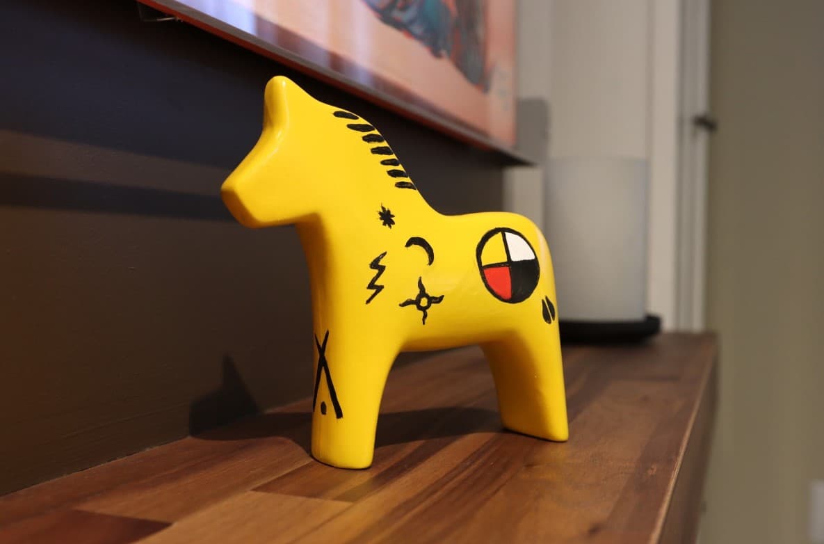 A yellow dala horse with black symbols marked on it's side sits on a wooden table.