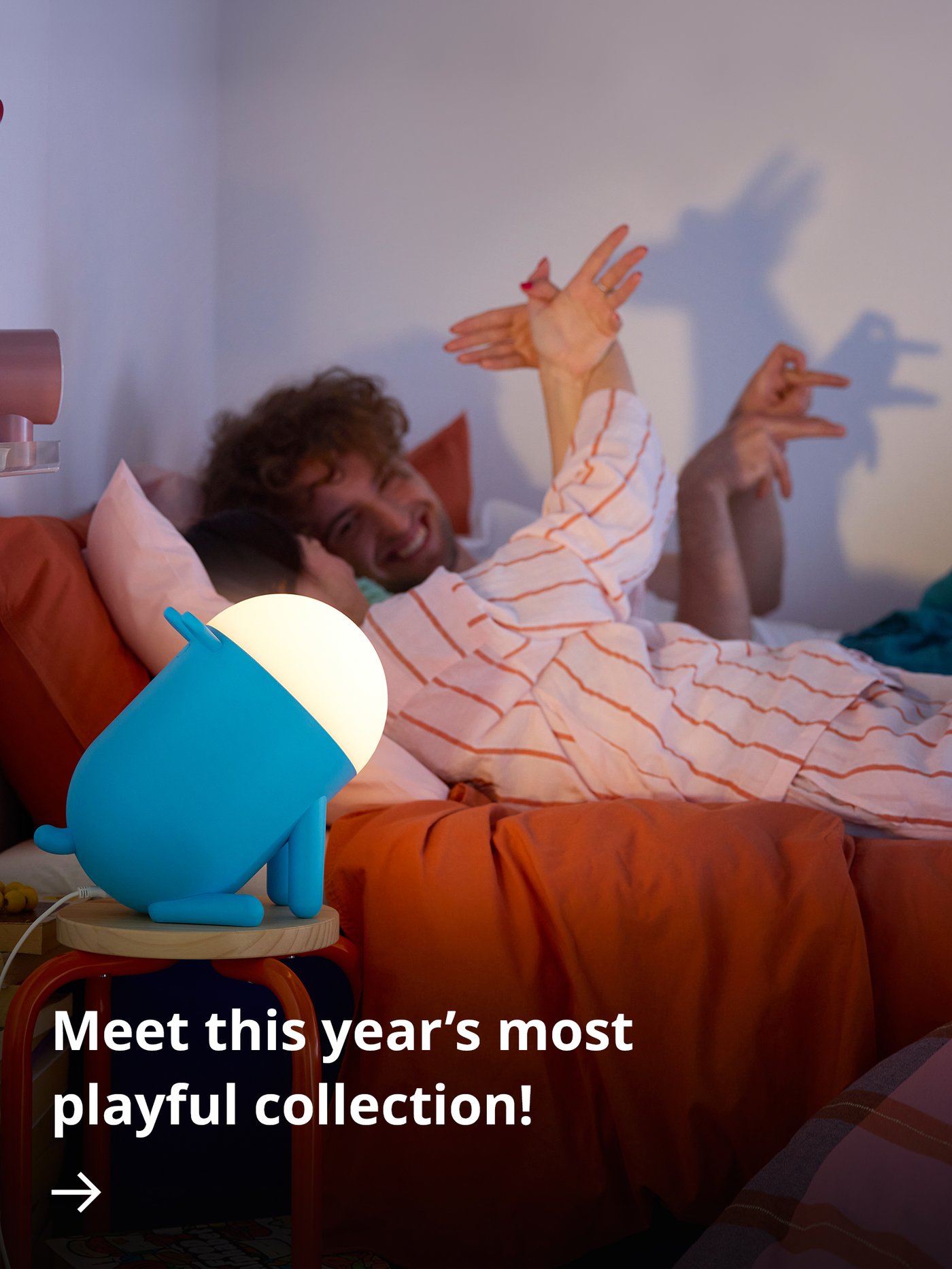 A yellow giraffe-shaped GREJSIMOJS floor lamp stands in a dark room beside a child’s bed.