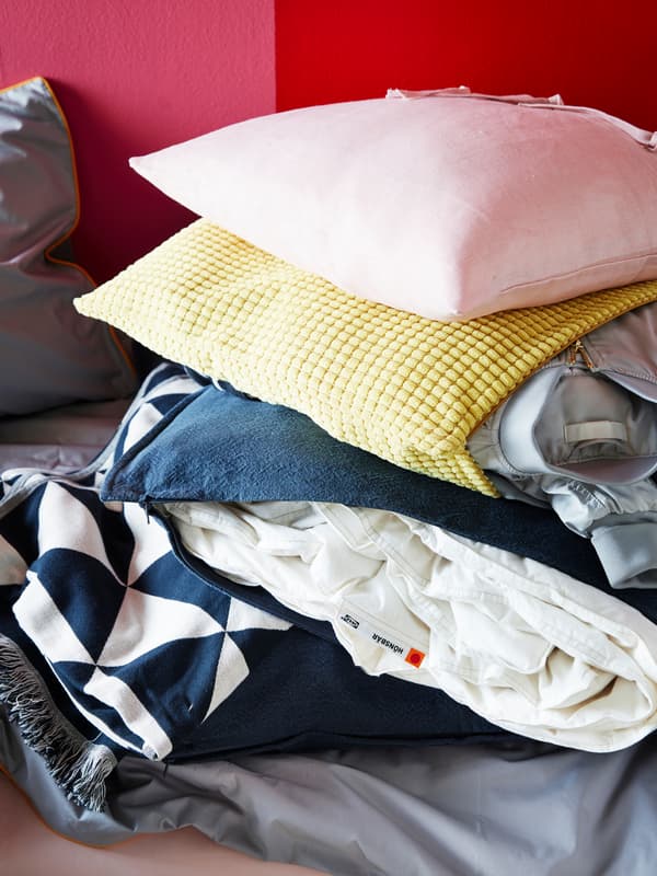 A yellow GULLKLOCKA cushion cover stuffed with a jacket and a blue cushion cover filled with a blanket for seasonal storage.