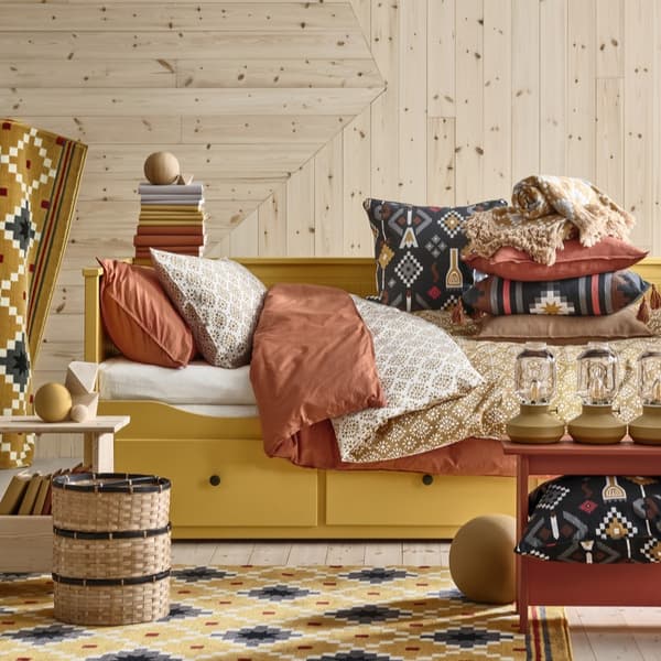A yellow HEMNES day-bed dressed with cushions, throws and bed linen. Among them, the new MOSSNYCKLAR and FRUKTMOTT cushions.
