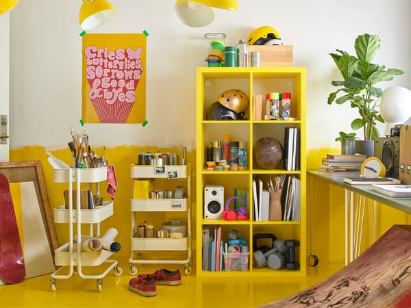 A yellow KALLAX shelving unit and two white RÅSKOG trolleys provide a lot of storage space in a yellow and white room.