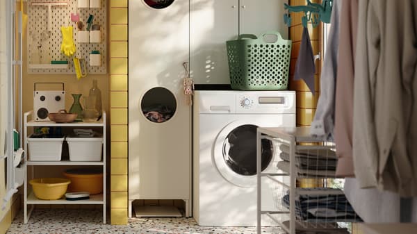 A yellow-tiled laundry room with a white NYSJÖN cabinet with a white washing machine and accessories in different colours.