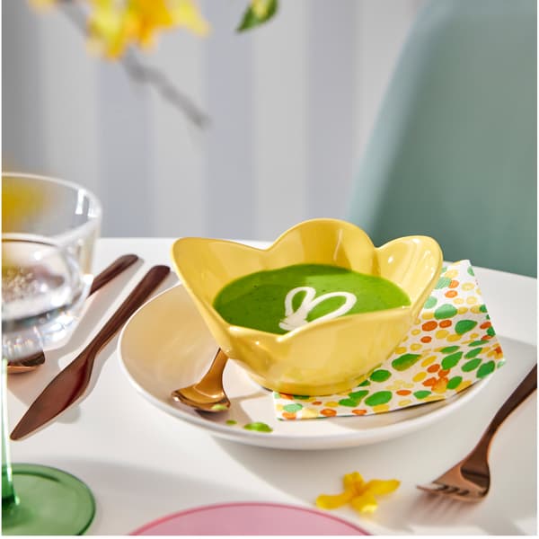 A yellow TJÄRLEK bowl with soup in it is placed on a dotted TJÄRLEK paper napkin which is in turn placed on a white plate.