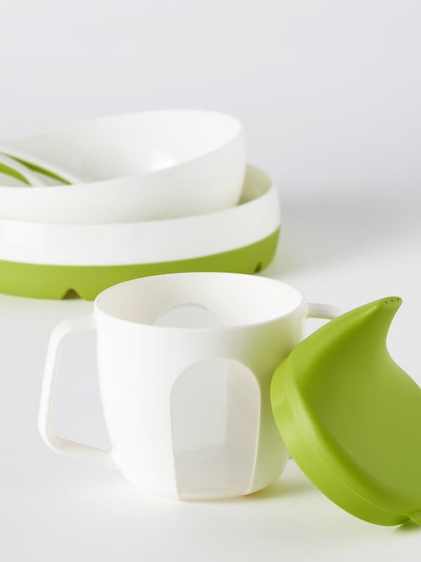 A young boy wearing a MATVRÅ bib sits in a highchair at a table with HEROISK bowls, plates, a mug and cutlery.