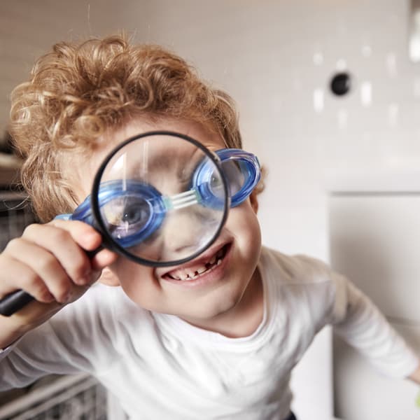 A young boy wearing swimming goggles looking through a magnifying glass smiling.