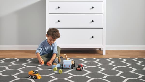 A young child playing with toys on a large, patterned rug next to a white HEMNES three-drawer chest.