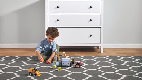 A young child playing with toys on a large, patterned rug next to a white HEMNES three-drawer chest.