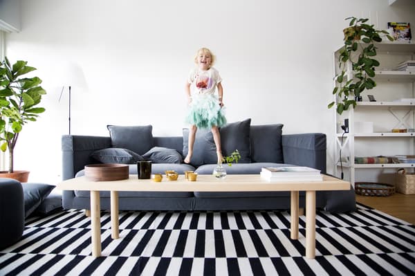 A young girl bouncing on a sofa in front of a coffee table in the living room.