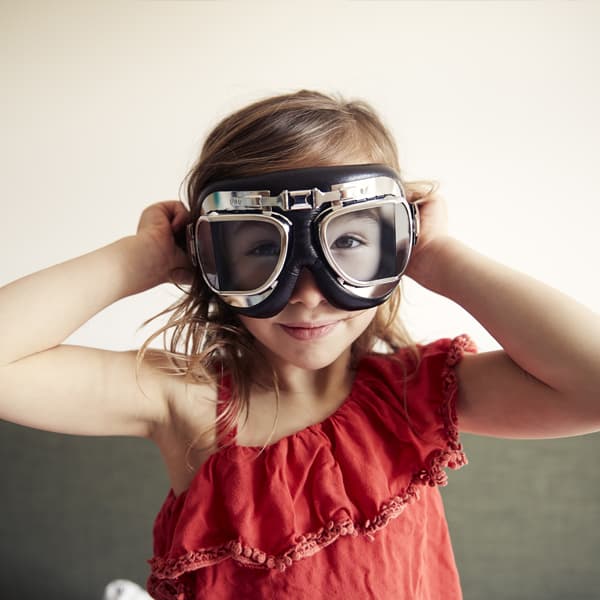 A young girl in a red shirt wearing large goggles.