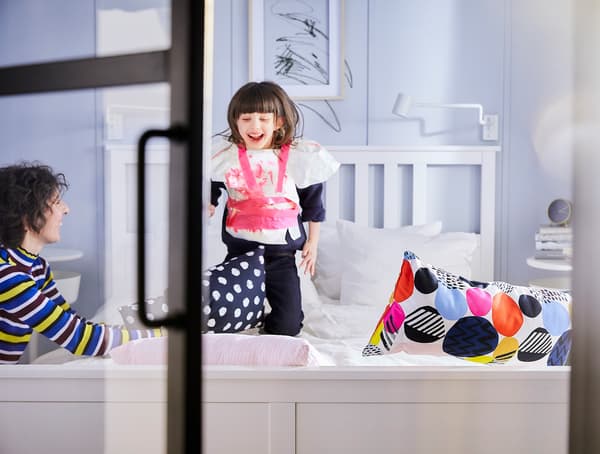 A young girl jumping on a white double bed.