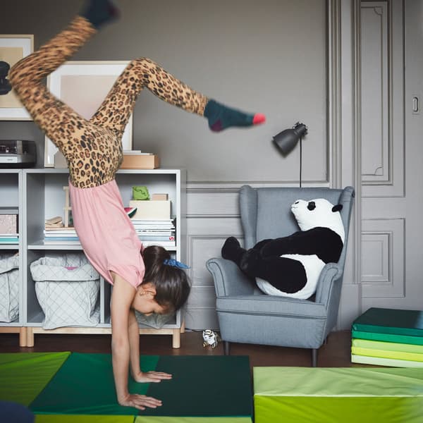 A young girl performing a handstand on an IKEA PLUFSIG green folding gym mat.