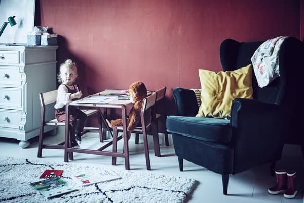 A young girl sitting at a children’s table in a red room.