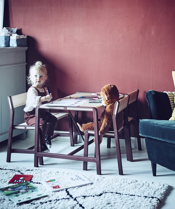 A young girl sitting at a children’s table in a red room.