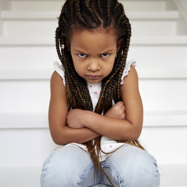 A young girl sitting on white stairs crossing her arms and pouting.